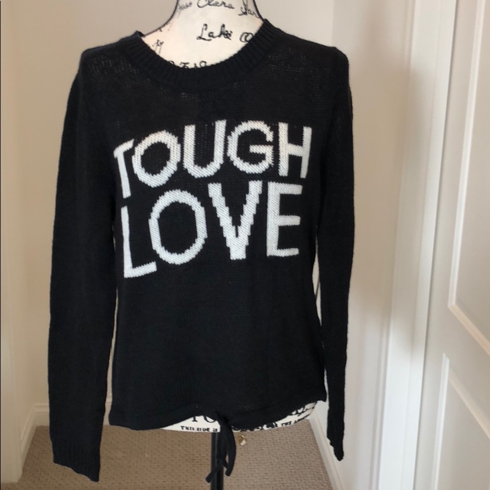 Black sweater drawstring bottom says “tough love”
